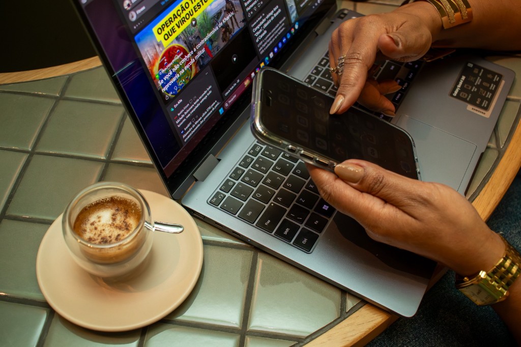 Mãos digitando em notebook com café, representando trabalho técnico e organização financeira
